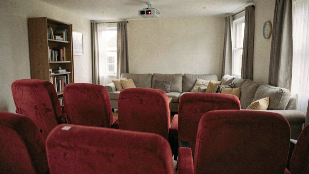 Fauteuils rouges d’une petite salle de cinéma faisant face à un salon avec vidéoprojecteur, montage photographique naturel sans écran lisible