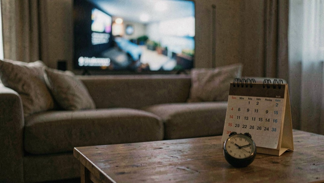 Canapé devant un écran volontairement flou, calendrier papier et minuteur posés sur une table basse, ambiance nocturne douce sans personne